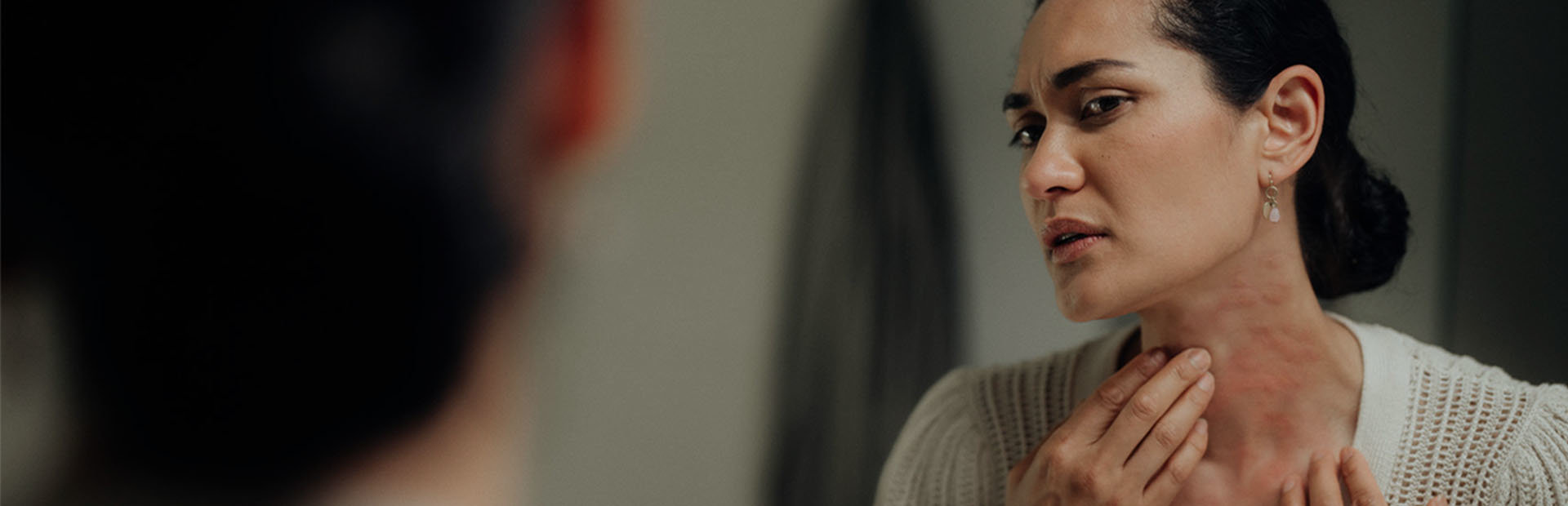 Middle-aged woman looking at hives on her neck in the mirror